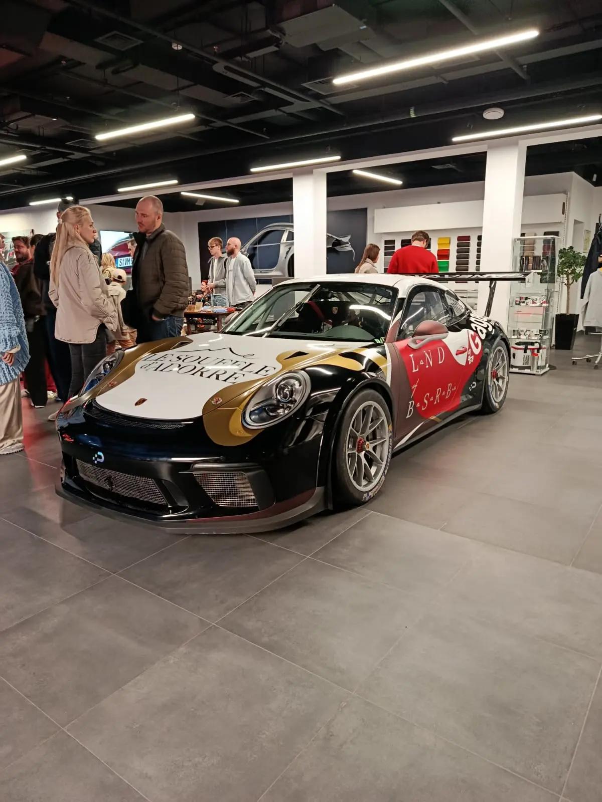 Гоночный 911 GT3 Cup в ливрее посреди шоурума, вокруг гости