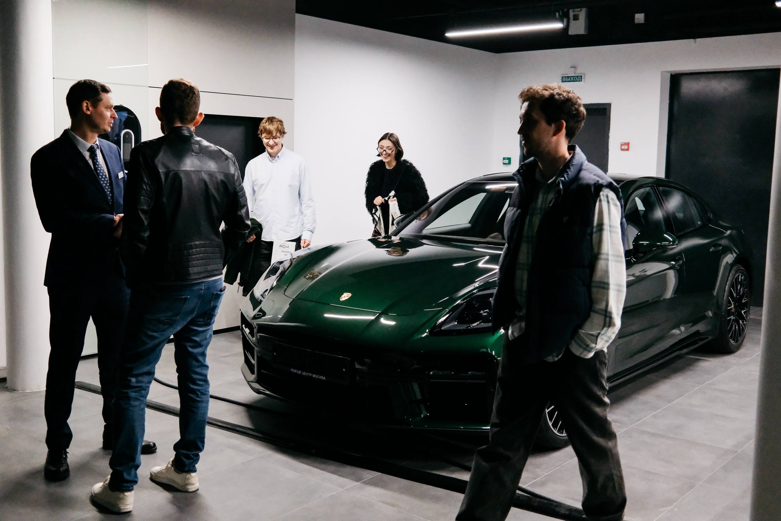 Тёмно-зелёная Panamera в светлом зале, рядом гости и менеджер PCM в костюме